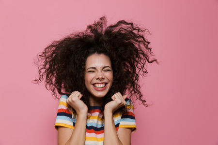 Image of joyous woman 20s with curly hair rejoicing and smiling isolated over pink backgroundの写真素材