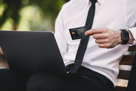 Cropped photo of handsome business man outdoors in the park using laptop computer holding credit card.の写真素材