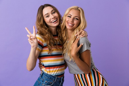 Two pretty young girls friends standing isolated over violet background, showing peaceの写真素材