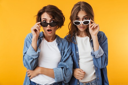 Photo of shocked excited emotional young women friends posing isolated over yellow background.の写真素材