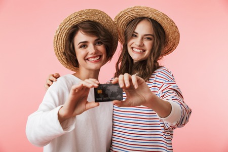 Image of happy cute young women friends posing isolated over pink background holding credit card.の写真素材