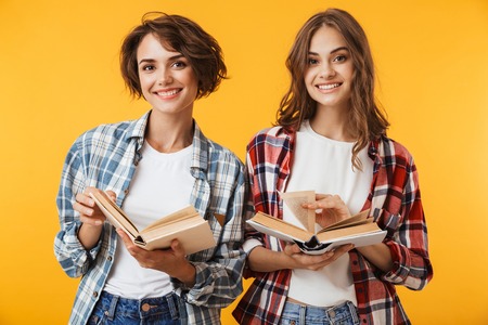 Photo of young women friends posing isolated over yellow background holding books.の写真素材
