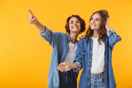 Image of amazing smiling emotional young women friends posing isolated over yellow background pointing.の写真素材