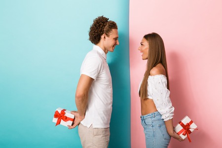 Portrait of a happy young couple hiding gift boxes behind backsの写真素材