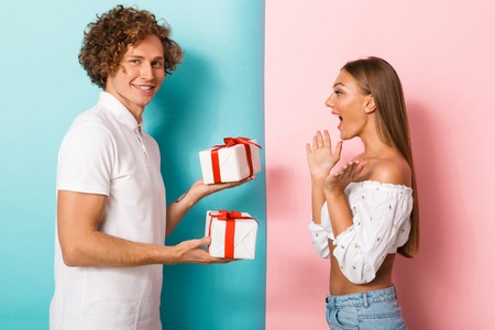 Portrait of a happy young couple standing over two colored background, man giving two present boxes to his girlfriendの写真素材