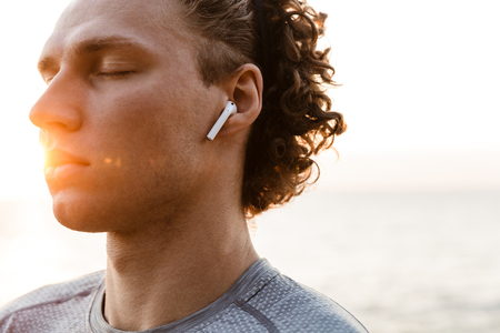 Image of handsome young sports man standing on the beach listening music with earphones.の写真素材