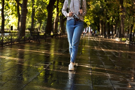 Cropped photo of young woman walking outdoors with backpack and camera.の写真素材