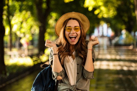 Image of excited shocked beautiful young happy woman walking outdoors with backpack.の写真素材