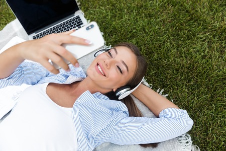Image of beautiful young pretty woman in park outdoors listening music using mobile phone.の写真素材