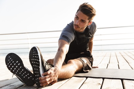 Image of young concentrated sports man outdoors on the beach make sport stretching exercises.の写真素材