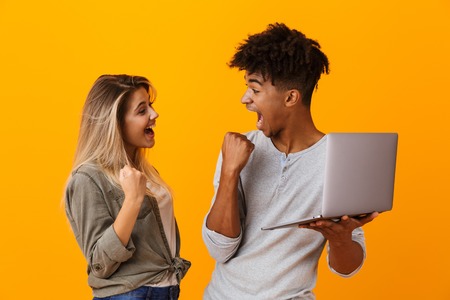 Photo of happy young loving couple standing isolated over yellow background using laptop computer...