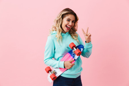 Image of caucasian girl 20s smiling and holding skateboard isolated over pink backgroundの写真素材