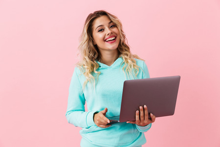 Image of european cheerful girl 20s smiling and holding silver laptop isolated over pink backgroundの写真素材