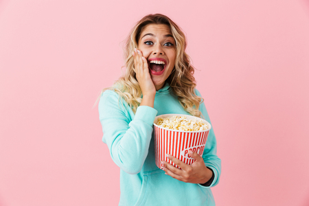 Image of happy young woman 20s holding bucket with popcorn and looking at camera isolated over pink backgroundの写真素材