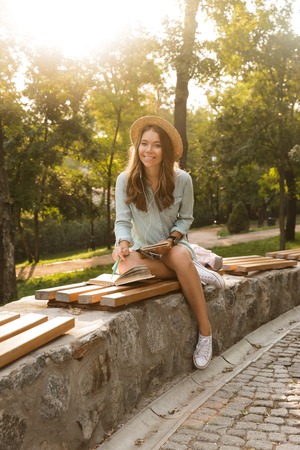 Smiling young teenage girl with backpack sitting outdoors, listening to music with earphones, studyingの写真素材