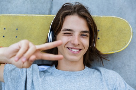 Top view of a cheerful young teenge boy spending time at the skate park, laying on a skateboard at a ramp, listening to music with headphonesの写真素材