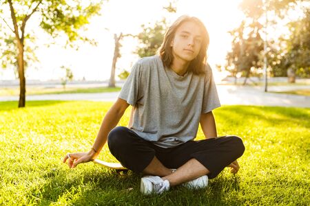 Image of handsome young guy sitting outdoors in the park on grass looking camera.の写真素材