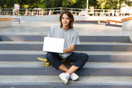 Image of handsome attractive young skater guy sit in the park using laptop computer.の写真素材