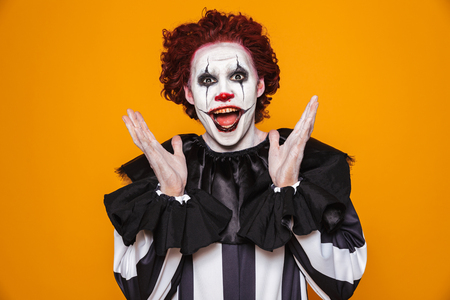 Funny man clown in costume looking camera with happiness isolated over orangeの写真素材
