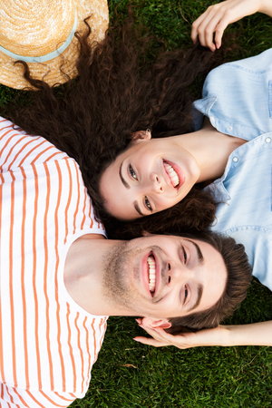 Image from top of beautiful couple man and woman 20s lying alongside opposite heads on green grass in parkの写真素材