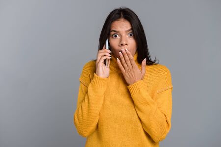 Image of a shocked surprised woman posing isolated over grey wall background talking by mobile...