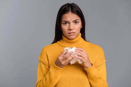 Image of ill woman standing isolated over grey wall background holding napkin.の写真素材