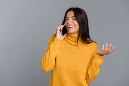Image of a happy woman posing isolated over grey wall background talking by mobile phone.の写真素材