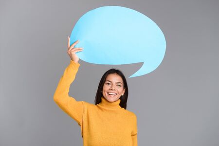 Image of a happy woman posing isolated over grey wall background holding speech bubble.