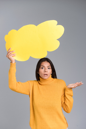 Image of a confused woman posing isolated over grey wall background holding thought bubble.の写真素材