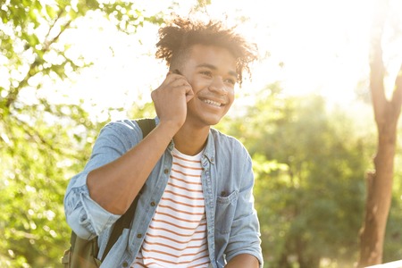 Image of handsome emotional young african guy in park outdoors talking by mobile phone.の写真素材