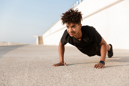 Confident young african man dressed in sportswear doing push-ups at the beachの写真素材