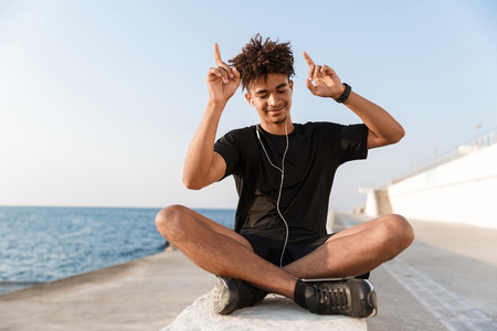 Smiling young african teenager at the beach, listening to music with earphones, dancingの写真素材