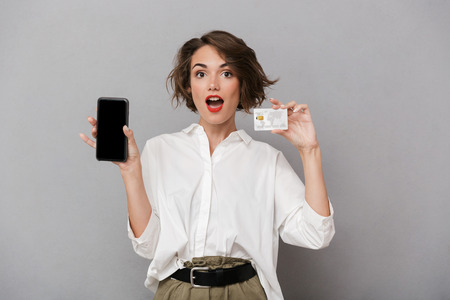 Photo of beautiful woman 20s holding mobile phone and credit card isolated over gray backgroundの写真素材