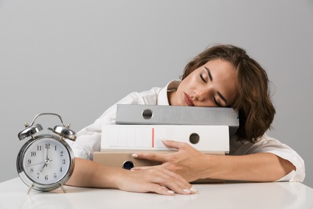 Image of young sleeping business woman isolated over grey wall background sitting at the table with folders.の写真素材