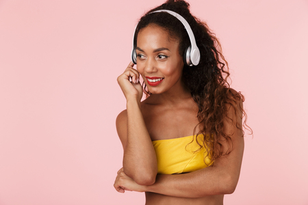 Image of young cheerful woman in swimwear posing isolated over pink background listening music with headphones.の写真素材