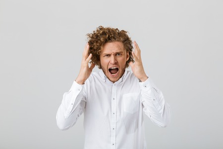 Portrait of an angry young man with curly hair isolated over white background, shoutingの写真素材