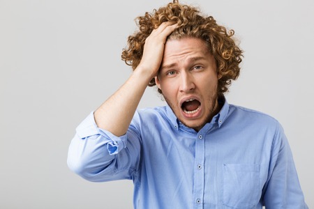 Portrait of a shocked young man wearing shirt standing isolated over gray background, screaming