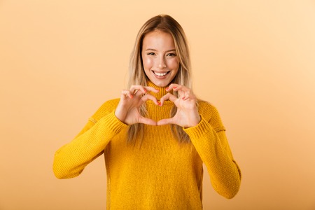 Portrait of a lovely young woman dressed in sweater standing isolated over yellow background,...