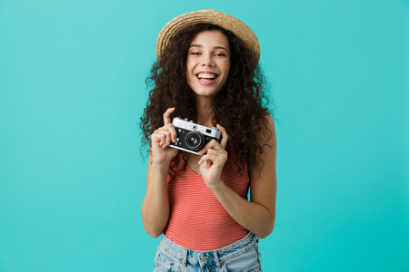 Portrait of young woman 20s wearing straw hat holding retro camera isolated over blue background