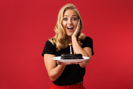 Image of young happy woman showing birthday sweetie on plate isolated over red background.の写真素材