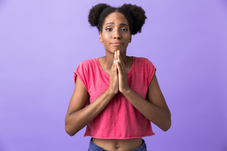 Photo of attractive african american woman keeping palms together for pray isolated over violet...