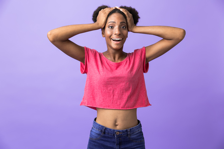 Photo of surprised african american woman shouting and grabbing head isolated over violet backgroundの写真素材