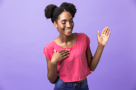 Photo of happy african american woman smiling and waving hand isolated over violet backgroundの写真素材
