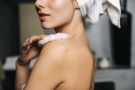 Beautiful young woman wrapped in bath towel standing at the bathroom, using powder puffの写真素材