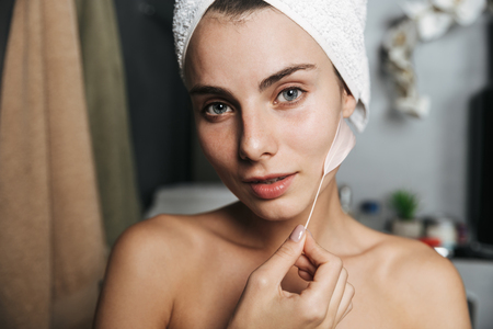 Close up of a beautiful young girl with towel wrapped around her head touching her skin with a feather at the bathroomの写真素材