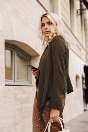 Beautiful young woman walking at the city, holding mobile phoneの写真素材