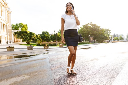 Image of a beautiful business woman walking outdoors talking by mobile phone.の写真素材
