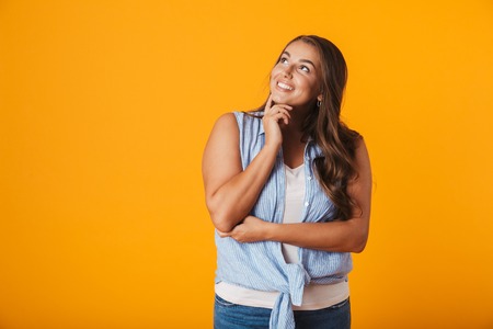 Happy young woman standing isolated over yellow background, looking awayの写真素材