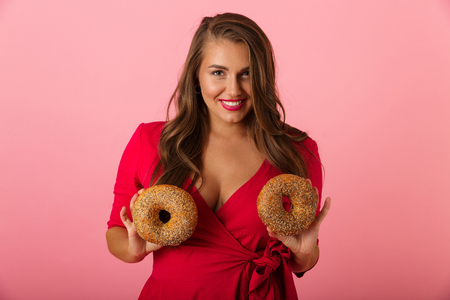 Image of a happy young woman isolated over pink wall background holding donuts.の写真素材