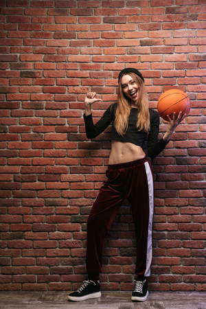 Full length photo of young sporty girl standing against brick wall with basketballの写真素材